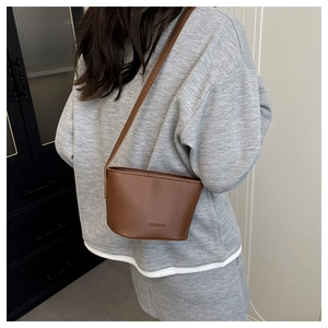 Detail shot of brown lychee grain leather crossbody bag with FASHION embossed logo