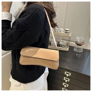 Detail view of beige patent leather baguette bag worn as a shoulder bag in cafe setting