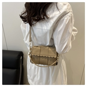 Close-up of woven crossbody bag with wavy flap edge and leather strap worn by a model