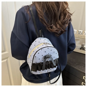 Detail of blue striped backpack with heart prints, black ruffles, and bow charm detail