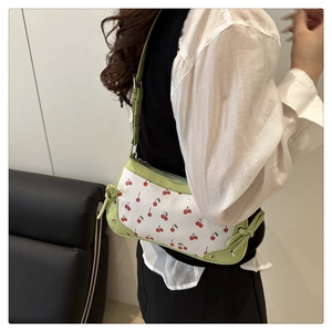 Close-up of cherry print shoulder bag with green trim shown on model at a side angle