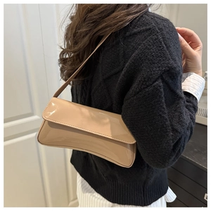 Gros plan du sac à bandoulière en cuir verni beige porté par un mannequin en style épuré