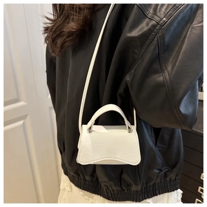 Detail showing white crocodile embossed leather mini bag with curved base and thin strap