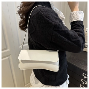 Detail shot of a white patent leather baguette bag worn over the shoulder by a model