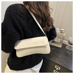 Sac baguette minimaliste en cuir verni beige porté à l'épaule par un mannequin