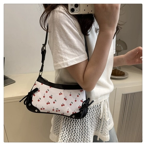 Detail view of white leather shoulder bag with red cherry prints and black bow accents
