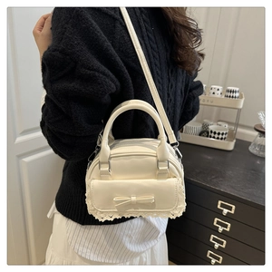 Detail showing cream-white Boston bag with delicate lace trim and bow on the side