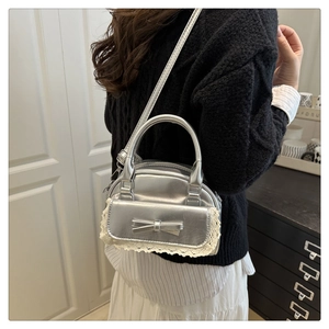 Silver bow shoulder bag featuring white lace trim and metallic finish in detail
