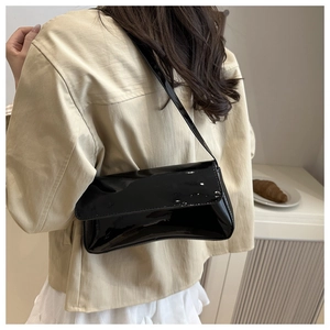 Side view of black patent leather baguette shoulder bag shown on model for size and gloss