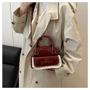 Close-up of burgundy patent leather bag with white lace trim and bow on beige trench coat