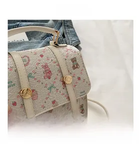 Close-up of white leather handbag with cute cartoon bear prints and golden metal buckle
