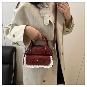 Detail of burgundy bowling bag with bow and lace trim on a model in a beige coat