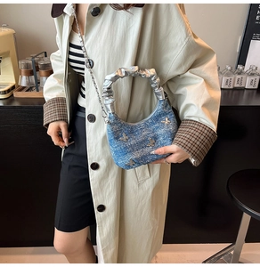 Blue denim bag with silver butterfly charms and pleated handle shown on a beige trench coat