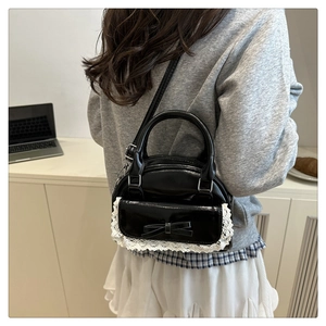 Detail of black glossy handbag with white lace trim and bow knot on office desk