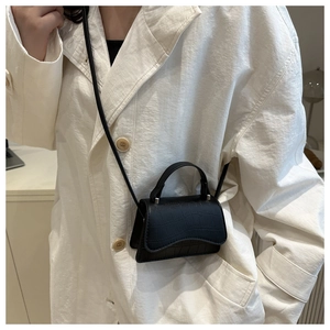 Detailed view of mini black faux crocodile leather crossbody bag on white blazer