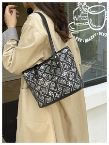 Woman in khaki trench coat carrying a black tote bag with silver geometric floral patterns