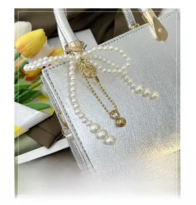 Close-up of metallic silver handbag with pearl bow charm and gold chain detail