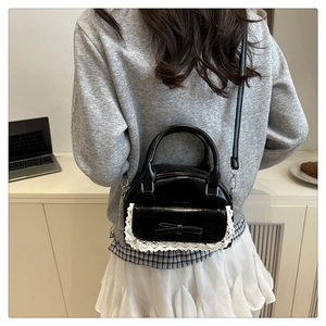 Detail of black glossy bowling bag featuring white lace trim and bow on a shoulder strap