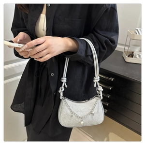 Detail of silver sequin shoulder bag with metal chain, pearl and heart charms on black shirt