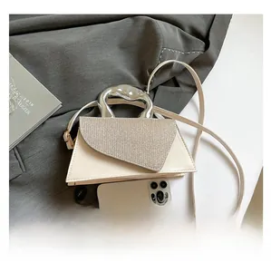 Detail of a cream trapezoidal handbag with rhinestone flap and silver metallic handle