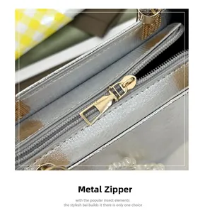 Detailed macro view of silver glossy handbag featuring a gold metal zipper and pearl trim