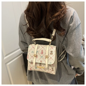 Detail of cream backpack with cartoon bear and strawberry prints worn on model's back