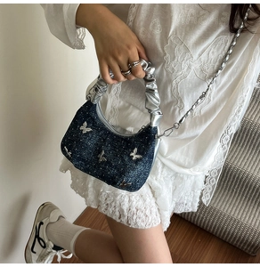 Detailed shot of denim dumpling bag with silver butterfly charms and chain strap