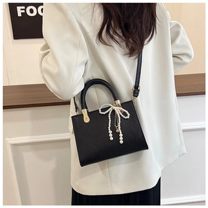 Detail of black crossbody bag with pearl bow charm and gold accents on white blazer
