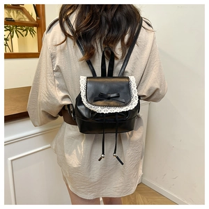 Detail of black mini backpack with lace trim and bow knot on smooth faux leather