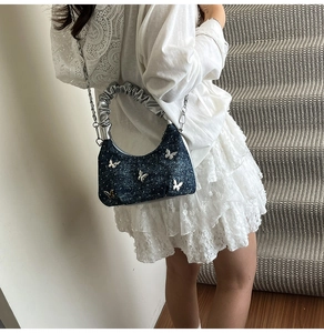 Detail of navy denim crossbody bag with silver butterfly studs and metal chain strap