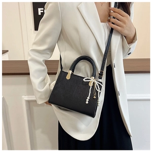 Detail of black textured handbag featuring a pearl bow charm and gold-toned metal hardware