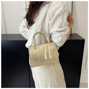Detail of golden metallic square bag with pearl bow charm and chain on a white sweater