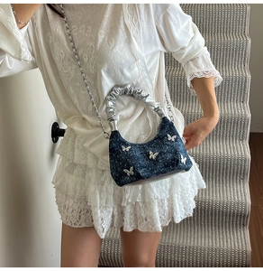 Detail of blue denim crossbody bag with metallic butterfly accents and sparkly finish