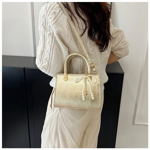 Detail of gold crossbody bag with pearl bow charm on model in minimalist interior