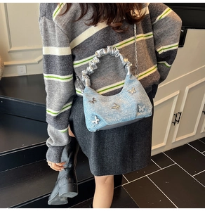 Detail of light blue denim purse with silver butterfly charms and pleated handle