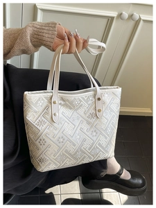 Detailed view of white tote bag featuring traditional geometric embroidery and rivets