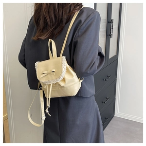 Detail of cream mini backpack with lace trim, bow decoration, and drawstring on model