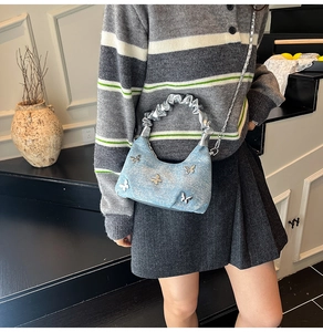 Detailed close-up of light blue denim bag with silver butterfly charms and pleated handle