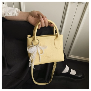Close-up of pale yellow PU leather handbag with litchi texture and pearl bow charm