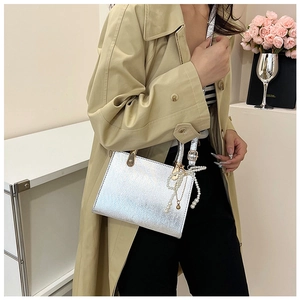 Detail of silver metallic handbag featuring pearl bow charm and gold hardware accents