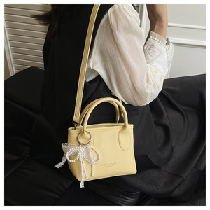 Bright yellow bucket bag with lychee texture and pearl lace bow detail shown on a model