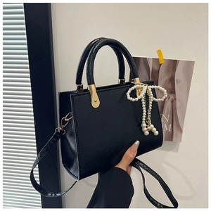 Detail of black textured PU leather handbag featuring a pearl bow charm and gold hardware