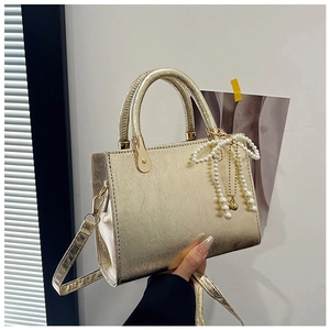 Detail view of gold metallic handbag with curved handle and pearl bow charm accessory