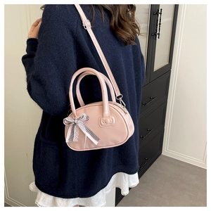 Detail of light pink mini bowling bag with bow embossing and lace charm worn on shoulder