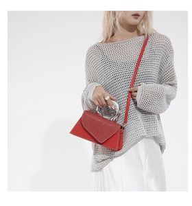 Detail of red crossbody bag featuring silver metal arc handle and glitter texture flap
