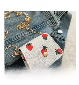 Detail of white strawberry print mini purse with gold chain on denim fabric background