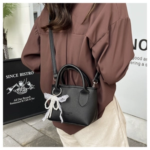 Outdoor shot of a black litchi leather mini bucket bag with a pearl lace bow charm