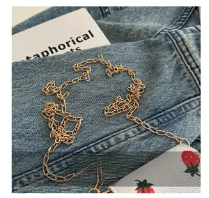 Close-up of a white strawberry print wallet with a gold chain strap on denim fabric