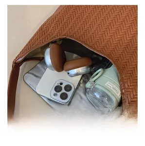 Spacious interior of brown woven shoulder bag holding tablet, phone, and headphones
