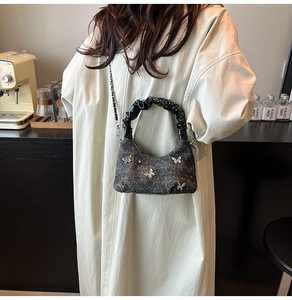 Detail of glitter handbag with silver butterfly accents and chain strap on shoulder